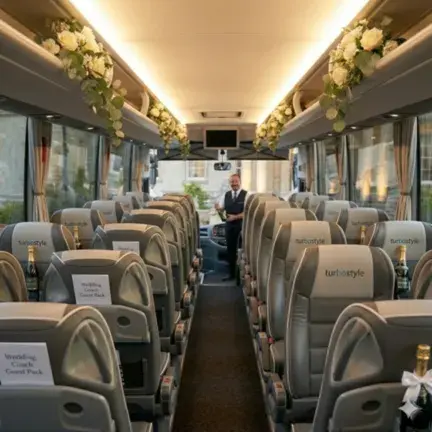 Interior view of a Turbostyle wedding coach featuring luxury leather seating, branded headrests, overhead floral arrangements, and complimentary champagne for wedding guests.